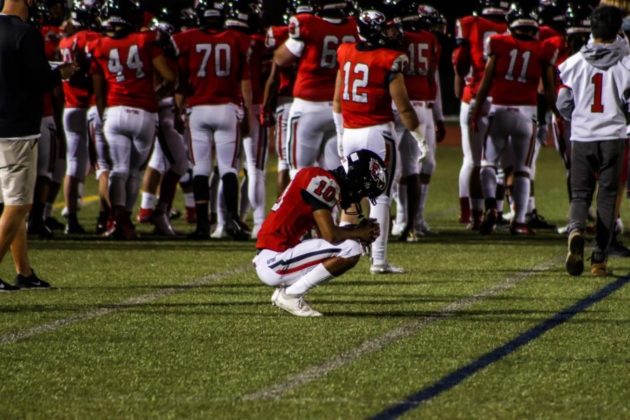 Week one, #10 Langston Williams (middle) crouches down on the sidelines while the team groups up to converse pregame.