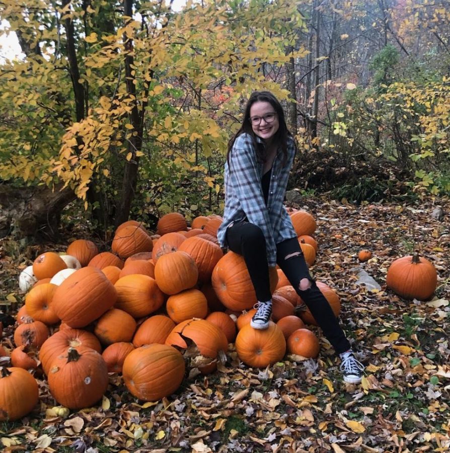 Shelby Anderson posing for a photo on a patch of pumpkins.