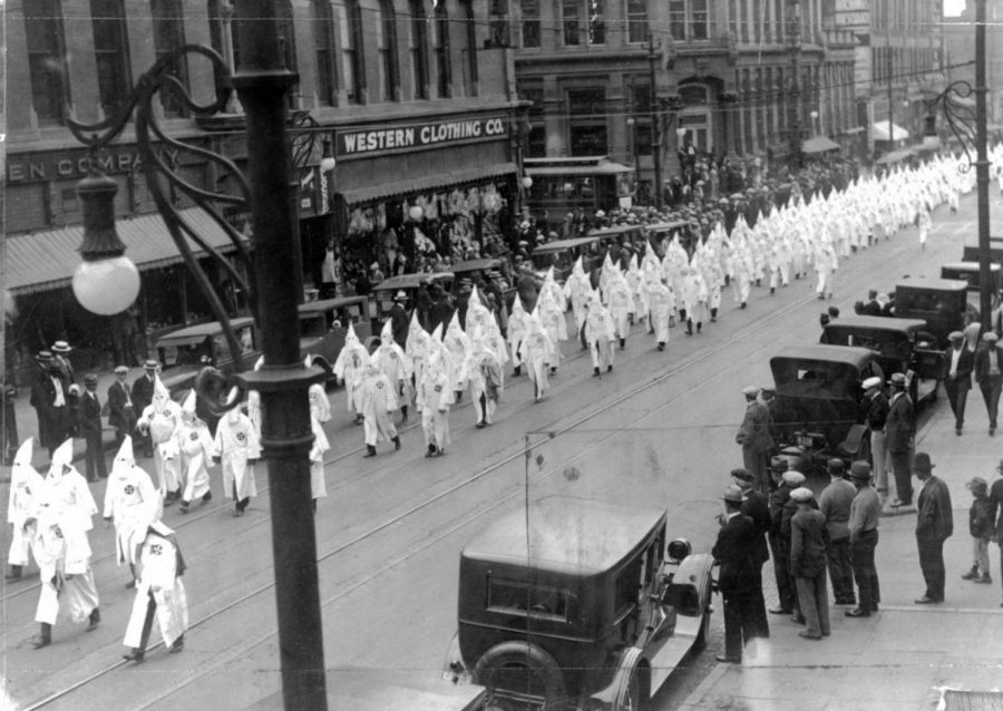 Denver Post archive photo- Members of the Ku Klux Klan march in a parade on Larimer Street in Denver, May 31, 1926. They wear hoods and robes as spectators look on. Parked automobiles line the street.”