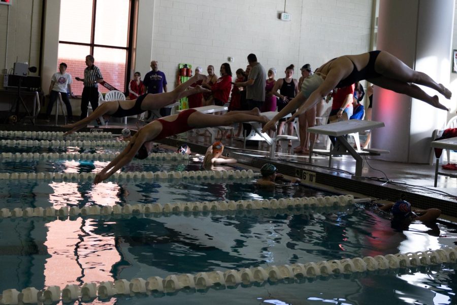 Freshman Sadie Halladay (in red) dives into the longest, most tiring event of the morning: the 500 yard freestyle.