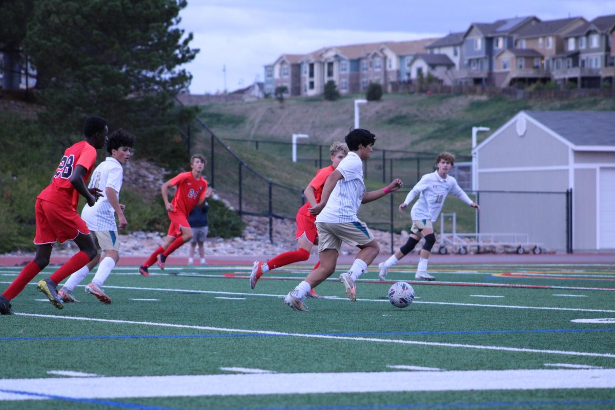 Several Eaglecrest players running along side the Mullen player who has possession of the ball.