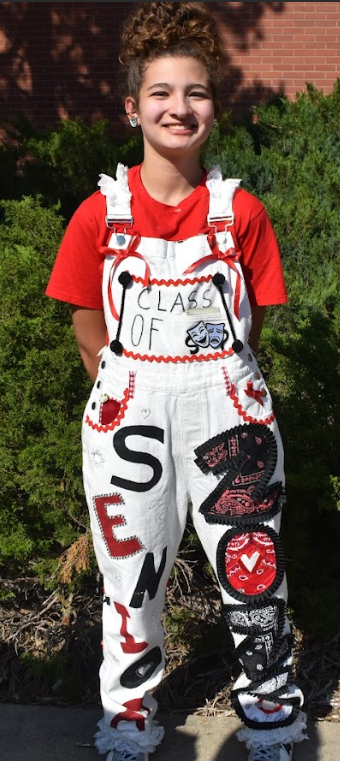 Evie Foster striking a pose with her personalized overalls, emphasizing the theatre masks patch on the front pocket. At Raptor Rally, she was working the drama club booth the entire night. "My favorite part is the frills on the 2026 contrasting with bandannas on the right side of my leg," said Evie Foster.